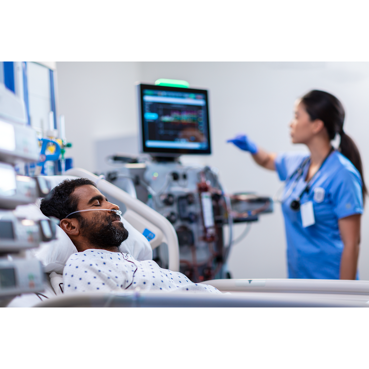 Focus on patient with nurse touching monitor in the background